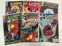 Photo of six Superman comic books arranged in two rows of three, showing cover art with Superman and other characters, covers show condition and plastic sleeves