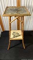 Full view of the vintage two tier side table showing the faux bamboo legs and painted floral foliage tops on both tiers.