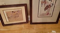Framed Asian artwork pair leaning against the wall on wooden floor showing both pieces and their bamboo-style frames.