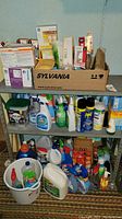 Full view of shelf with multiple boxes of light bulbs on top and a variety of cleaning supplies on middle and bottom shelves.