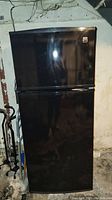 Full view of Kenmore Coldspot black refrigerator with top freezer section, placed against basement wall.