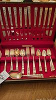 Front view of silverplate flatware set with multiple utensils arranged vertically and horizontally inside a red storage case.