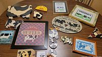 Overview of all cow-themed decor items laid out on a table including cut-outs, framed prints, plaques and door stop