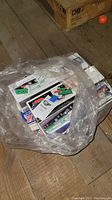 Plastic bag containing multiple Hess toy truck boxes on a wooden floor.