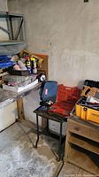Photo showing metal shelf with multiple toolboxes, cans, and hand tools scattered around and on the shelf.