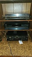 Three stacked audio components inside wooden shelving unit: Panasonic stereo receiver at bottom, Onkyo CD player in middle, Technics turntable on top.