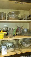Kitchen cabinet shelf showing nested glass bowls, glass jars, and plastic lids