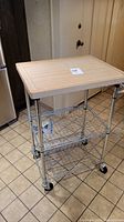 Full view of metal rolling cart with butcher block top in tile floor kitchen area.