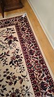 Close-up image showing the border and floral patterns of the beige area rug with red and blue design.