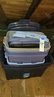 Stacked plastic storage totes in multiple colors and sizes shown from above and side angles in attic.