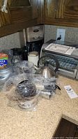 Full view of kitchen appliances including toaster oven, kettle, coffee maker, and pots, all placed on kitchen counter