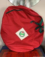 Red circular storage bag for Christmas wreath, heavy gauge canvas material, with zipper and green tie. Patch sewn on bag with decorative wreath design and 'Lot #39 Top' inscription.