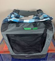Front of soft-sided foldable pet crate with mesh zipper door and blue checkered pyjamas on top