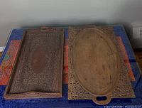 Both rectangular and oval rosewood trays placed side by side on a colorful tablecloth, showing overall size and shape differences as well as carved detail.