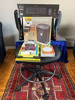 Office chair with assorted office electronics and accessories stacked on the seat, including keyboard/mouse set box, paper shredder box, software boxes, and other accessories.