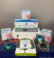 Canon and HP printers with three boxes of refill ink kits on each side, a single HP ink cartridge, paper pack, and two USB cables in front.