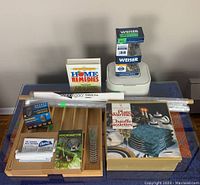 Photo shows the full assortment of items including the Royal Doulton plate warmer box, bamboo utensil organizer, pest repellent devices, compost container, shower curtain rings, window films, hygrometer, and other accessories arranged on a table.