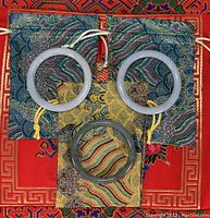 Three jade bangles on silk brocade pouches, showing different colors and rounded shapes.