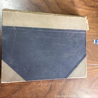 Closed hardcover book with black and brown cover placed on wooden surface.