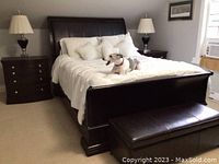 Full view of bed with pillows and bedding, two nightstands with lamps, and bench at foot of bed.