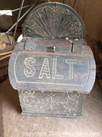 Front view of salt box with hinged curved lid open, carved 'SALT' inscription on front door and sunburst motif on inside lid.