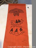 Orange burlap banner with black ink prints depicting an owl and abstract animal silhouettes, signed Nanocak