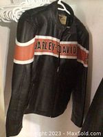 Photo showing front side of the black Harley Davidson leather jacket with orange and white stripes and brand name across chest.