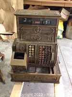Front and top view of ornate brass cash register showing keys, drawer slot and amount display