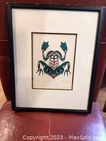 Front view of the framed Indigenous art print titled "Frog" showing the stylized frog design in green, red, and black ink with a white mat and simple black frame.