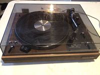 Entire turntable with closed clear dust cover and wood-grain base.