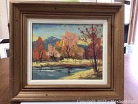 Front view of oil painting showing colorful landscape with trees, water, and hills, framed.