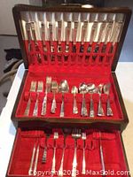 Full view of silverplate flatware set organized inside a wooden chest with red velvet lining. The flatware includes forks, spoons, and various serving utensils, majority arranged in upright slots.