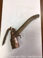 Side view of vintage brass gas pump handle showing curved spout and lever.