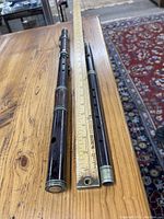 Two disassembled wooden flutes laid on a wooden table with measuring ruler showing lengths around 13 to 17 inches, showing dark rosewood bodies and basic keywork.