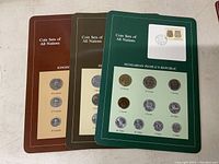 Three vintage international coin sets mounted on colored cards: Kingdom of Lesotho, Republic of Indonesia, and Hungarian People's Republic. Each card has coins with denomination labels.
