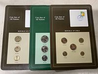 Three different international coin sets, each mounted and labeled by country and denomination with stamps.