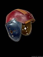 Front and side view of the antique leather football helmet showing maroon, tan, and blue leather panels and ventilation holes.