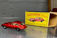 Red diecast E Type Jaguar model with original yellow box upright behind it.