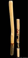 Two didgeridoos displayed side by side on a dark backdrop, showing size difference and natural/painted finishes.