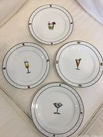 Four appetizer plates displayed showing four different cocktail-themed designs on white plates.