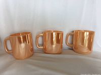 Three vintage peach luster mugs placed side by side showing their front and side profiles against a plain white background.