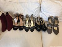 Front view of five pairs of ladies' shoes, showing different styles from ankle boots to ankle-strap sandals and heels in red, black, metallic silver, and grey.
