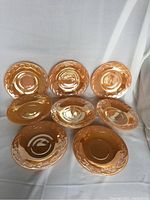 Eight peach lustre saucers arranged on a white draped background showing a glossy laurel leaf design around the center well area.