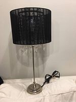 Full view of the contemporary glam table lamp with chrome base, black shade, and hanging crystals.
