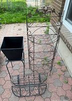Full view of multi-tiered bronze metal plant stand, black square plastic planter in metal frame, and two metal railing-style planters with rust.
