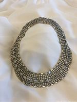 Full view of rhinestone collar-style necklace laid flat on white fabric showing overall shape and sparkle.