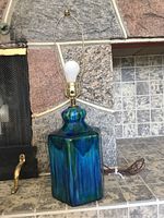 Vintage blue ceramic lamp on a tiled stone surface from a front angle showing the ceramic base, brass socket, and harp without shade.
