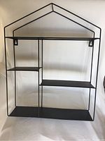 Front view of the black metal wall-mountable shelf shaped like a house with three shelves of different sizes