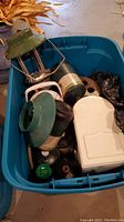Photo of blue bin containing green Coleman lantern, white and red coolers, green propane tanks, and other camping equipment.