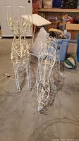 Two white wireframe reindeer Christmas decorations with light bulbs wrapped around. Untested with repaired cords visible.